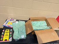 Box and plastic-wrapped green Uline mop heads with catalog and safety label sheet