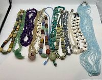 All 13 necklaces laid flat showing variety of stones, colors and pendants