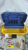 Open Flambeau tackle box showing empty blue tray and loose lures, bobbers and packaged tackle surrounding