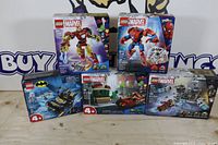 Group shot of five boxed LEGO sets – three Marvel, two DC