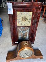 Front view of both clocks, wall clock standing upright, mantel clock in front