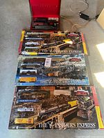 Three boxed Insider’s Express train sets, red carry case above, loose power supply visible