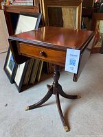 Table closed with one leaf down, showing drawer front, pedestal, brass feet.