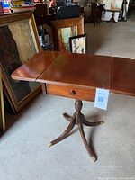 Full view of drop-leaf table opened showing pedestal base and brass-capped legs