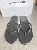 Top view of black flip flop sandals in front of branded box
