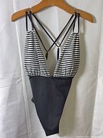 Front view of black and striped one-piece swimsuit on hanger