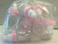 Bag containing 12 clear plastic mini baby bottles with pink caps and white nipples