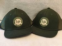Front view of two identical olive green L&P children’s baseball hats showing LP patch logos and brims