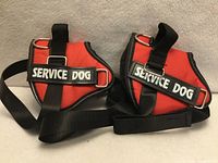 Front view of two red service dog harnesses showing patches, D-rings and straps