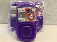 Front view of three packaged purple Goodbyn snack containers showing lids and product labels