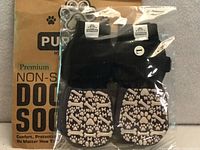 Front view of sealed package showing four black dog socks with beige grip pattern