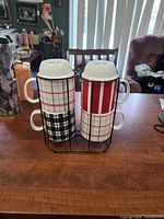 Front view of four patterned mugs stacked in black metal rack
