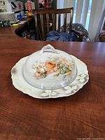 Angled view of covered butter dish showing floral decoration and embossed plate rim