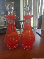 Front view of both red/orange glass decanters with stoppers