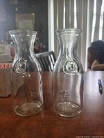 Front view of both clear glass milk bottles showing embossed logos