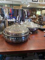 Both silver-plated covered dishes side by side showing ornate lids and glass bases