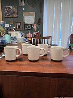 Front view of four beige speckled stoneware mugs on tabletop