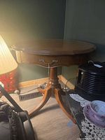 Full view of round pedestal side table showing drawer pull and pedestal base