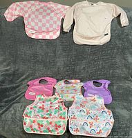 Full group of seven toddler bibs arranged on grey surface