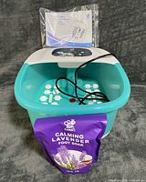 Top view of turquoise foot spa with lavender foot soak packet and power cord, manual behind