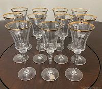 Front angled view of 11 crystal wine glasses showing faceted bowls, gold rims, stems and bases