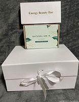 Front view of three boxed items: Energy Beauty Bar, Natural Amor bath set, white gift box with ribbon