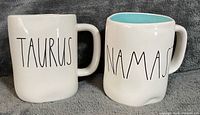 Front view of both mugs showing "TAURUS" and "NAMAS" text, white exteriors, turquoise interior visible on right mug