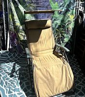 Full view of beige/tan outdoor lounge chair showing cushion, armrests, canopy and frame