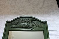 Close-up of carved duck motif on green wood frame