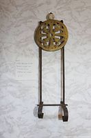 Full view of trivet showing brass top, iron frame, hanging loop and feet