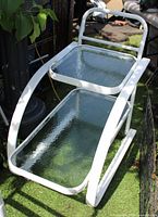 Full view of white metal two-tier side table with glass shelves