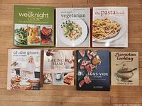 Overview of all seven cookbooks laid out on wooden floor