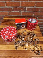 Overview of three red tins and pile of stainless-steel cookie cutters