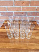 Twelve clear cylindrical beer glasses on wooden surface