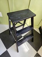 Front angled view of folded-out black two-step stool showing overall design and condition