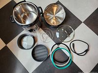 All components laid out: cooker base with stainless pot, pressure lid, glass lid, springform pan, steam basket, trivet, three sealing rings, power cord