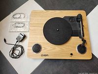 Top view of ION Archive LP turntable showing wood veneer plinth, felt mat, built-in speakers, ION logo, power adapter and accessories