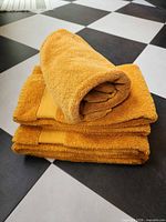 Stacked mustard cotton towels showing colour and terry texture