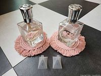 Pair of clear glass Lampe Berger lamps on pink macrame coasters with two plastic funnels