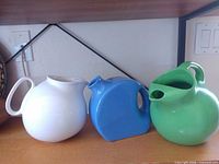Three ceramic pitchers in blue, green, white on shelf