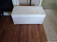Front angled view of closed white wicker chest on floor