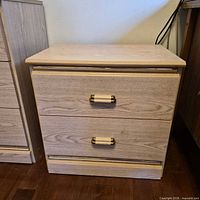 2-drawer nightstand showing light oak finish and brass-tone hardware