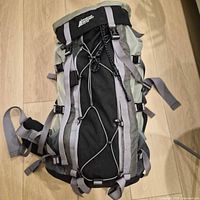 Front view of MEC backpack showing black front panel, gray compression straps, front bungee cord