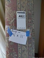 Rolled 8' x 11' oriental-style rug showing red blue beige pattern and label