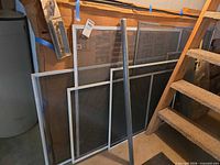 Group of aluminum window screens leaning against wall, assorted sizes