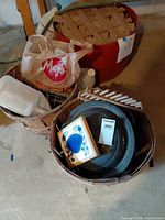 Overview showing wicker baskets with enamelware pans, plastic jug, bag, and red plastic tub with wooden lattice lid