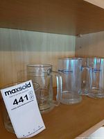 Three clear glass beer mugs, two with Bud Light logo, one unbranded, on wooden shelf