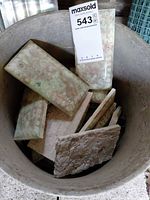 Bucket containing assorted green iridescent ceramic tiles and stone pieces with lot tag visible