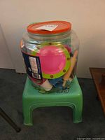Green plastic chair holding clear jar filled with multicolor plastic play dishes