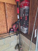 Trimmer leaning in shed with battery and charger visible on ledge